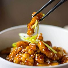 someone is holding chopsticks over a bowl of food with sesame seeds and meat