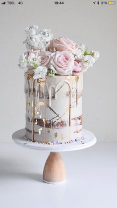 a white and gold cake with flowers on the top is sitting on a wooden stand