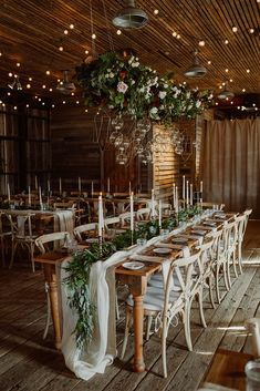 a long table set up with white chairs and greenery on the tables for an event