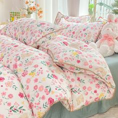 a bed covered in pink and green floral comforter next to a teddy bear on a table