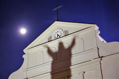 the shadow of a person standing in front of a building with a clock on it