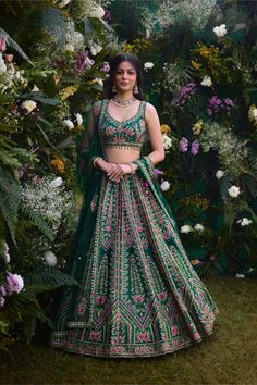 a woman in a green and pink lehenga standing next to some white flowers