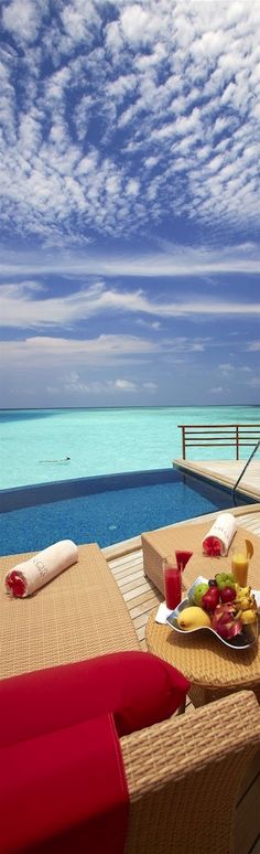 a table with fruit and juice on top of it near an ocean side deck that overlooks the water