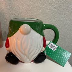 a green and white coffee mug with a santa clause on it's face, sitting next to a package