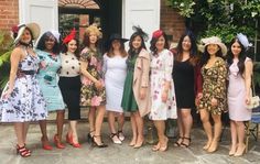 a group of women standing next to each other in front of a building wearing dresses and hats