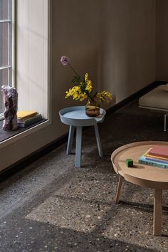 two tables with books and flowers on them next to a window sill in a living room