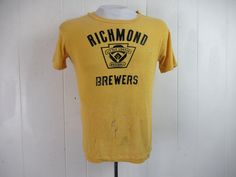 "Vintage 1960s yellow cotton t shirt with black graphics: Richmond Brewers Little League Baseball. Made by Southern Athletic. Size small. Actual measurements are: 38\" around the chest 38\" around the waist 17.5\" shoulder seam to shoulder seam 23\" overall length In \"wrecked\" condition with several holes." Vintage Fitted T-shirt With Letter Print, Retro Yellow T-shirt With Letter Print, Retro Yellow T-shirt With Graphic Print, Yellow Retro T-shirt With Graphic Print, Vintage Cotton Pre-shrunk T-shirt, Retro Yellow Short Sleeve T-shirt, Yellow Retro Short Sleeve T-shirt, Retro Yellow T-shirt With Screen Print, Fitted Yellow T-shirt With Graphic Print