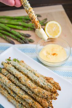 asparagus sticks being dipped with parmesan cheese and seasoning next to lemon wedges