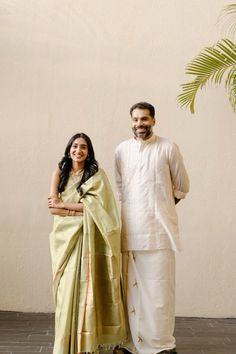 a man and woman standing next to each other in front of a wall with palm tree