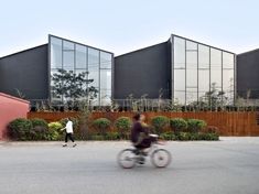 two people riding bikes on the street in front of some large black and red buildings