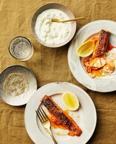 two white plates topped with food next to bowls of rice and lemons on a table