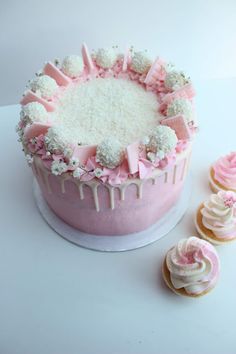 a pink cake and cupcakes on a white table