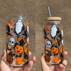 two hand painted halloween mason jars with pumpkins and ghost faces on them, one is holding a straw