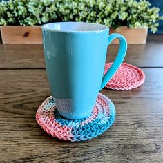 a blue cup sitting on top of a wooden table next to a crocheted coaster