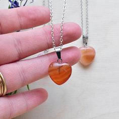 This necklace is made from a carnelian stone which has been cut into a puffy heart. The stone hangs from a silver plated chain. You can choose the length of the necklace you prefer. You will get a necklace at random. Please note that all necklaces are handmade and may differ from the pictured. The picture shows multiple necklaces. You will receive one necklace with one pendant. Ewelina Pas Jewelry Orange Heart Beads Jewelry For Gift, Heart-shaped Orange Necklace For Gift, Orange Jewelry With Heart Beads For Gifts, Gift Carnelian Crystal Necklace In Orange, Orange Heart Charm Jewelry, Heart-shaped Orange Jewelry For Gift, Orange Carnelian Crystal Necklace As Gift, Orange Carnelian Crystal Necklace For Gift, Orange Carnelian Crystal Necklace Gift