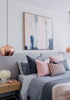 a bed with pink and grey pillows in a bedroom next to a painting on the wall