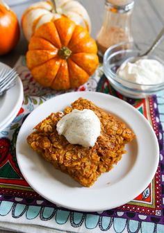 a white plate topped with two pieces of cake next to pumpkins and whipped cream