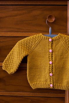 a yellow knitted sweater hanging on a wooden dresser next to a blue toothbrush