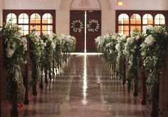 an aisle decorated with flowers and greenery in front of two doors that lead into the building