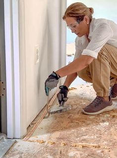 a woman is working on the floor in front of an open door with a power drill