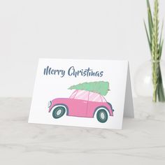 a pink car with a christmas tree on the roof is sitting next to a plant