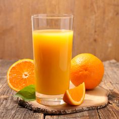 an orange juice in a glass next to sliced oranges on a wooden board with leaves