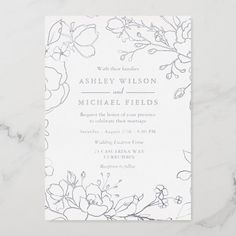 a wedding card with flowers and leaves on the front, in grey ink against a white marble background