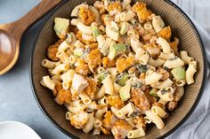 a bowl filled with macaroni and cheese on top of a table next to two wooden spoons