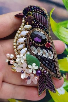 a bird brooch with beads and jewels on it's back in someones hand