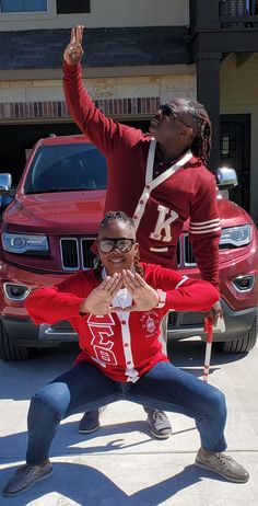 two people posing for a photo in front of some cars and one is holding his hand up