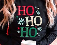 a woman is holding a coffee cup and wearing a black sweatshirt with the words oh hoo on it