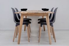 a wooden table with four black chairs and a bowl on top of it, against a white wall