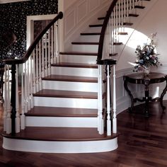 there is a white and brown staircase in the house with flowers on the table next to it