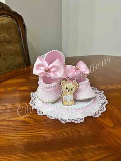 a small teddy bear sitting on top of a pink baby bootie cake with lace