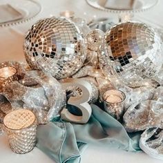 disco balls and candles on a table with silver napkins, tea lights and other decorations