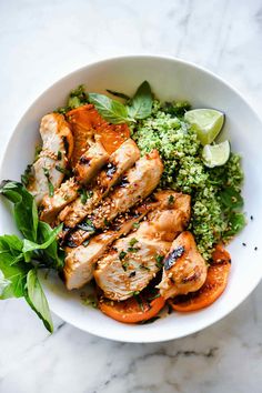 a white bowl filled with meat and vegetables on top of a marble counter next to a green leafy garnish