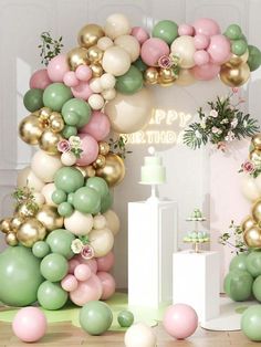 an arch made out of balloons and greenery is decorated with pink, green and gold balloons