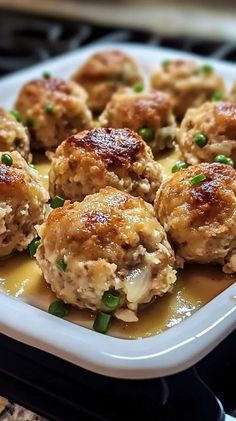 some meatballs with sauce and green onions in a white dish on top of a stove