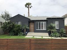 a gray house with palm trees in the front yard and grass on the side walk