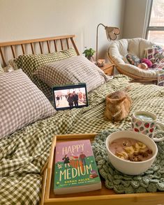 a cat sitting on top of a bed next to a bowl of cereal and a book