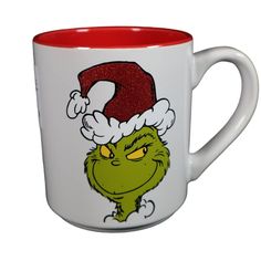 a white and red coffee mug with the grin face on it's side, wearing a santa hat