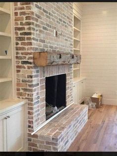 an empty living room with a brick fireplace and built - in shelving units on either side