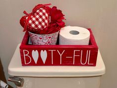 a toilet with two rolls of toilet paper and a heart shaped box on the lid