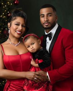 a man in a red suit holding a baby next to a woman wearing a red dress