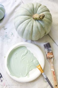 a white plate topped with green paint next to a small pumpkin and a painting brush