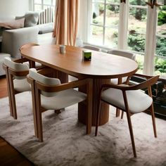 a dining room table with four chairs and a couch in front of large windows that look out onto the yard