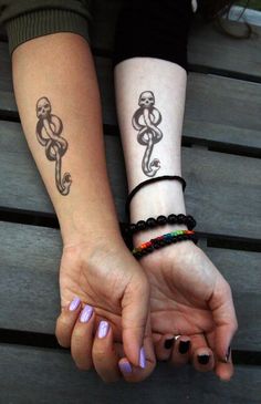 two people holding hands with tattoos on their arms and wrist, both wearing bracelets