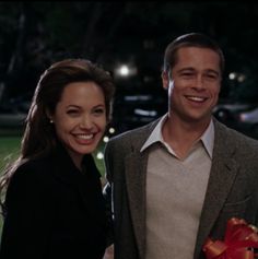 a man and woman standing next to each other in front of a tree with lights