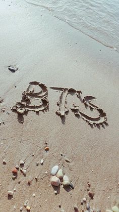 there is a word written in the sand at the beach with shells and pebbles around it