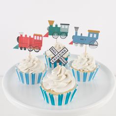 four cupcakes with white frosting and train decorations on top, sitting on a plate